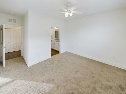 Indiana, Boone County, Lebanon Apartments for rent Empty bedroom with beige carpet, white walls, ceiling fan, and an open doorway leading to a bathroom with a double sink vanity. See all available apartments for rent at Hickory Cottages in Indiana Boone County Lebanon, Hickory Cottages has rental units ranging from 664-1420 sq ft