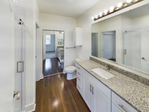 Indiana, Boone County, Lebanon Apartments for rent Modern bathroom with wood flooring, white cabinets, granite countertop, large mirror, shower stall, and toilet; mirrored closet doors visible in adjacent room. See all available apartments for rent at Hickory Cottages in Indiana Boone County Lebanon, Hickory Cottages has rental units ranging from 664-1420 sq ft