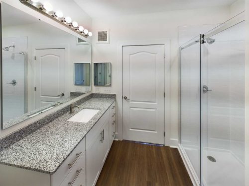 Indiana, Boone County, Lebanon Apartments for rent Modern bathroom with granite countertop, large mirror, double cabinet, glass-enclosed shower, and wooden floor. Bright lighting above the mirror. See all available apartments for rent at Hickory Cottages in Indiana Boone County Lebanon, Hickory Cottages has rental units ranging from 664-1420 sq ft