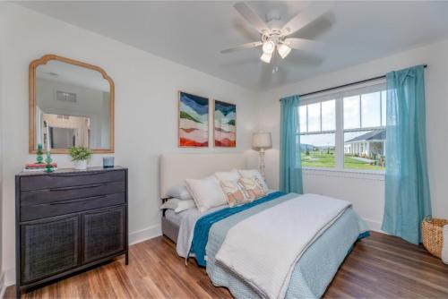 Apartments in Lebanon, IN A bedroom with a double bed, blue and white bedding, a black dresser with a mirror, and a window with blue curtains. There are two framed artworks above the bed and a ceiling fan overhead.