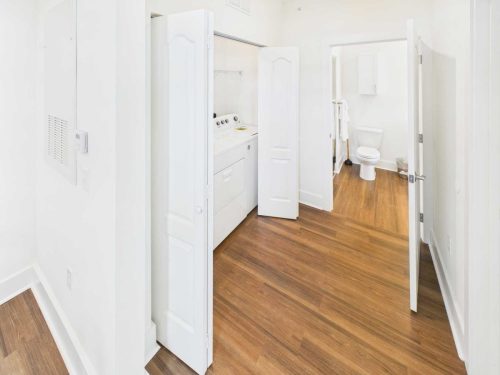 Indiana, Boone County, Lebanon Apartments for rent A laundry closet with a washer and dryer is adjacent to a bathroom with a toilet, towel rack, and trash can. The space has white walls and wood flooring. See all available apartments for rent at Hickory Cottages in Indiana Boone County Lebanon, Hickory Cottages has rental units ranging from 664-1420 sq ft