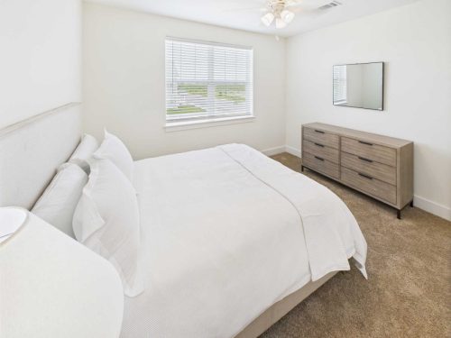 Indiana, Boone County, Lebanon Apartments for rent A bedroom with a neatly made bed, a window with blinds, a ceiling fan, a wall mirror, and a wooden dresser on a carpeted floor. See all available apartments for rent at Hickory Cottages in Indiana Boone County Lebanon, Hickory Cottages has rental units ranging from 664-1420 sq ft