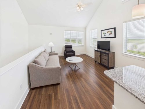 Indiana, Boone County, Lebanon Apartments for rent A bright living room with a gray sofa, armchair, round coffee table, TV on a wooden stand, and wood flooring. Multiple windows let in natural light. See all available apartments for rent at Hickory Cottages in Indiana Boone County Lebanon, Hickory Cottages has rental units ranging from 664-1420 sq ft