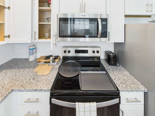 Indiana, Boone County, Lebanon Apartments for rent A modern kitchen with white cabinets, a microwave, an electric stove, baking trays, cutting boards, and a toaster on a granite countertop. Some cabinet doors are open. See all available apartments for rent at Hickory Cottages in Indiana Boone County Lebanon, Hickory Cottages has rental units ranging from 664-1420 sq ft