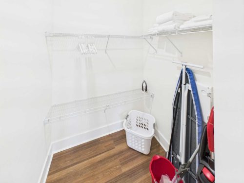 Indiana, Boone County, Lebanon Apartments for rent A laundry room with wire shelves, hangers, folded towels, a laundry basket, an ironing board, and a mop set on a wood floor. See all available apartments for rent at Hickory Cottages in Indiana Boone County Lebanon, Hickory Cottages has rental units ranging from 664-1420 sq ft