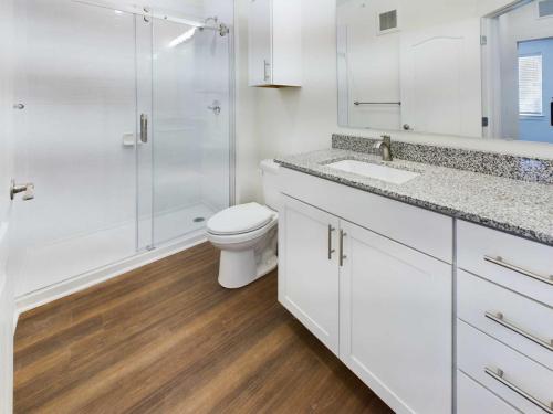 Apartments in Lebanon, IN Modern bathroom with a white vanity and granite countertop, wood flooring, toilet, and glass-enclosed shower.