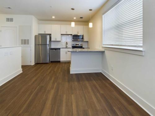 Apartments in Lebanon, IN Modern kitchen with stainless steel appliances, white cabinets, gray countertops, and wood flooring. Two pendant lights hang over the countertop. White blinds cover a window on the right wall.