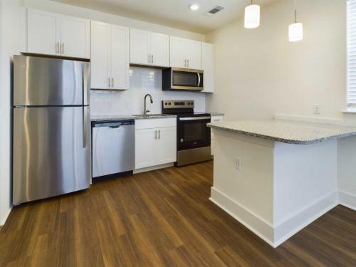 Apartments in Lebanon, IN Modern kitchen with stainless steel appliances, white cabinets, granite countertops, a double-basin sink, and a breakfast bar with pendant lighting on a hardwood floor.