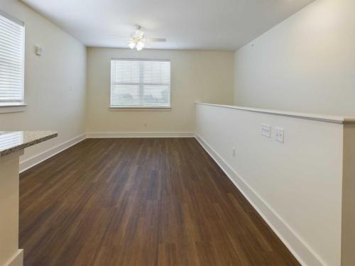 Apartments in Lebanon, IN A room with wood flooring, white walls, a ceiling fan, two windows with blinds, and a half wall with electrical outlets.