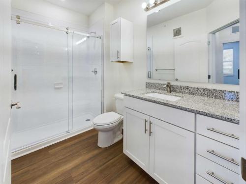 Apartments in Lebanon, IN A bathroom with a glass-enclosed shower, white vanity with a granite countertop, sink, toilet, and wood-look flooring.