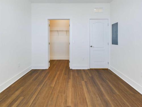 Apartments in Lebanon, IN Empty room with light-colored walls and wood flooring; features a closed white door, an open closet door with shelving, and an electrical panel on the right.