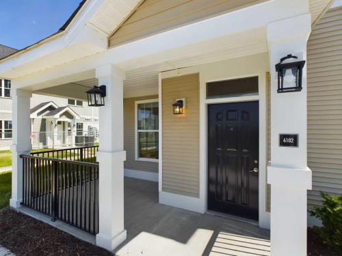 Apartments in Lebanon, IN Front porch of a house with beige siding, white trim, and a black front door. The porch is supported by white columns and features black lantern-style light fixtures. House number 6102 is visible.