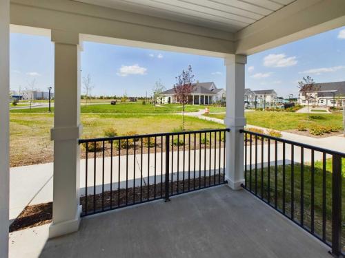 Apartments in Lebanon, IN View from a covered porch with black railings overlooking a neighborhood with green lawns, sidewalks, houses, and a playground in the distance under a clear blue sky.