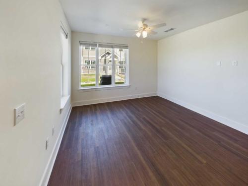 Apartments in Lebanon, IN An empty room with wooden floors, white walls, a ceiling fan, and a large window showing an outdoor view.