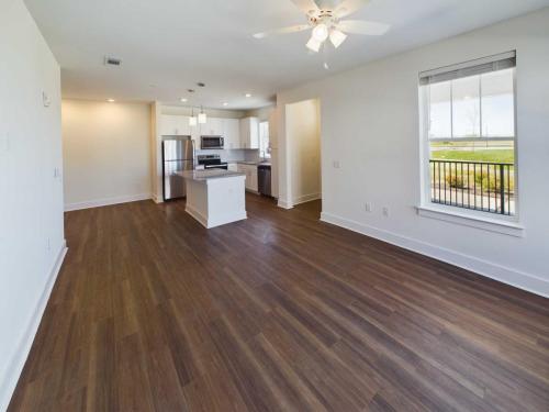 Apartments in Lebanon, IN Modern, unfurnished open-concept living area with hardwood floors, ceiling fan, large window, and kitchen with white cabinets, stainless steel appliances, and an island.