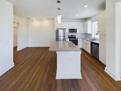 Apartments in Lebanon, IN Modern kitchen with white cabinets, stainless steel appliances, and a large granite island. The space features wooden flooring and recessed lighting.