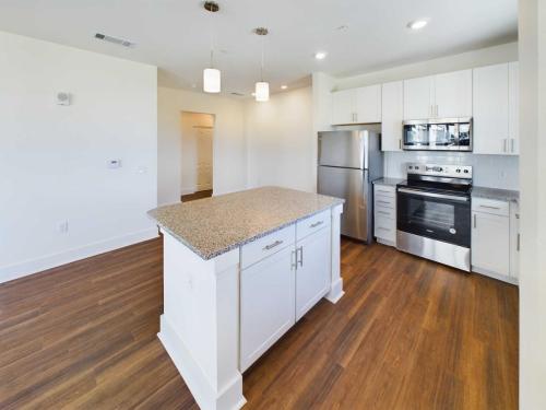 Apartments in Lebanon, IN Modern kitchen with white cabinets, stainless steel appliances, granite countertops, a central island with pendant lighting, and hardwood floors.