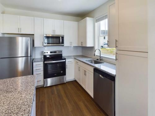 Apartments in Lebanon, IN Modern kitchen with stainless steel appliances including a refrigerator, oven, microwave, and dishwasher. White cabinets, granite countertops, and wooden flooring are also visible.