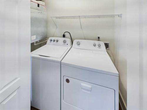 Apartments in Lebanon, IN A laundry room with a white top-loading washing machine on the left and a matching dryer on the right, under a wire shelf.