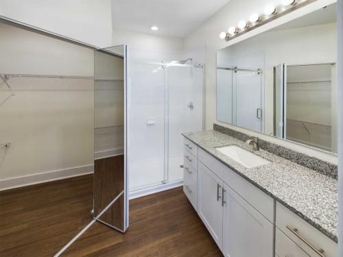 Apartments in Lebanon, IN Modern bathroom with a large vanity featuring a granite countertop and single sink, glass-enclosed shower, mirrored medicine cabinets, and wooden flooring.