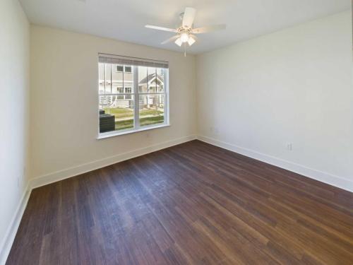 Apartments in Lebanon, IN A vacant room with light-colored walls, a ceiling fan, hardwood flooring, and a large window overlooking a yard.