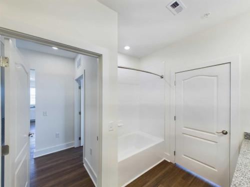 Apartments in Lebanon, IN A bathroom with a white bathtub, glass shower door, and wooden flooring. The image also shows doors leading to other rooms.