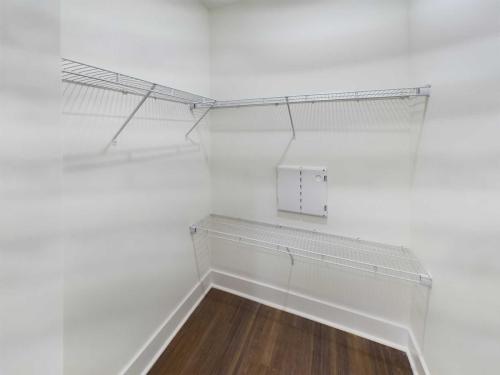 Apartments in Lebanon, IN A small, empty closet with white walls features three wire shelves and a wooden floor. A rectangular electrical panel is mounted on the back wall.