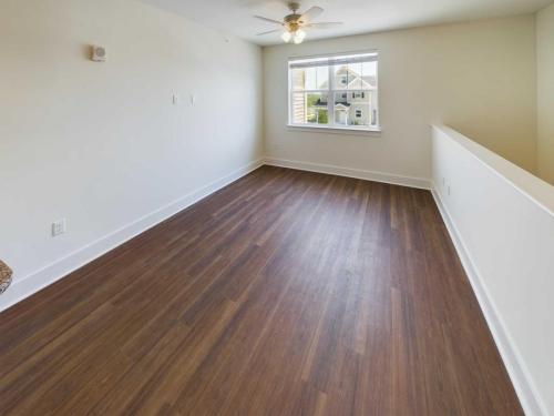 Apartments in Lebanon, IN A bright, unfurnished room with wood flooring, a white wall, a ceiling fan, and a window offering views of neighboring buildings. Ideal for those seeking Apartments For Rent in Lebanon Indiana.