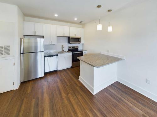 Apartments in Lebanon, IN A modern kitchen with white cabinets, stainless steel appliances, and granite countertops. It includes a refrigerator, stove, microwave, dishwasher, and a kitchen island with pendant lighting. Perfect for those seeking Apartments For Rent in Lebanon Indiana.