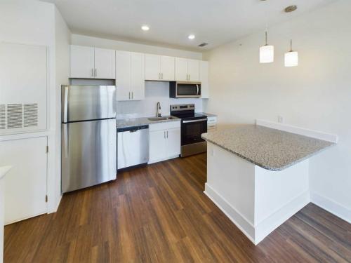 Apartments in Lebanon, IN A modern kitchen in these Apartments For Rent in Lebanon Indiana features white cabinets, stainless steel appliances, and a granite countertop island with two pendant lights. The floor has a wood-like finish.