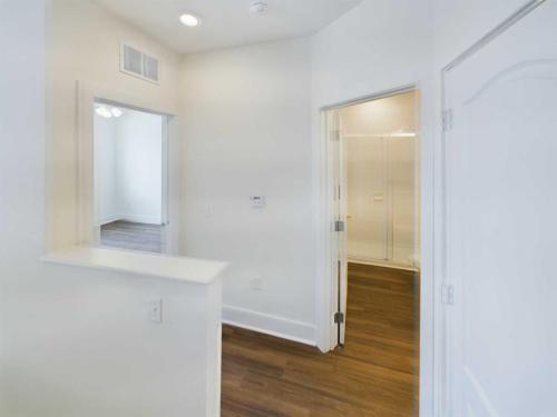 Apartments in Lebanon, IN A small interior hallway with wooden flooring and white walls leads to two rooms, one featuring an open door revealing a shower, and another room with a ceiling fan. This charming detail can be found in the available apartments for rent in Lebanon, Indiana.