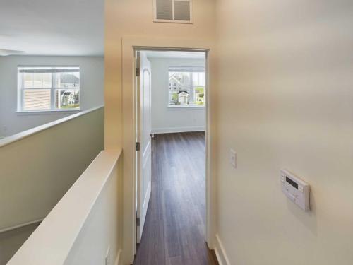 Apartments in Lebanon, IN Interior view showing a hallway in one of the apartments for rent in Lebanon, Indiana, leading to a room with large windows, white walls, and wooden flooring. An air vent is on the upper wall near the ceiling, and a white door is partially open.