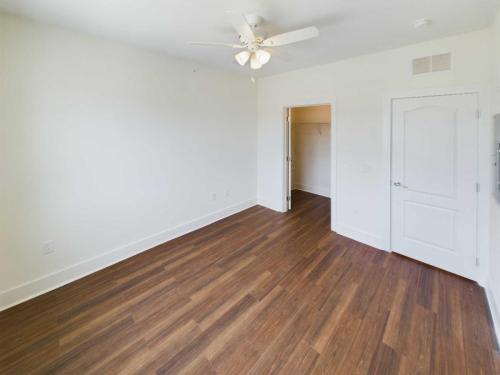 Apartments in Lebanon, IN Empty room with hardwood flooring, a white ceiling fan, and white walls. There is a door leading to a walk-in closet and another door closed to the right side. Perfect for those searching for apartments for rent in Lebanon, Indiana.