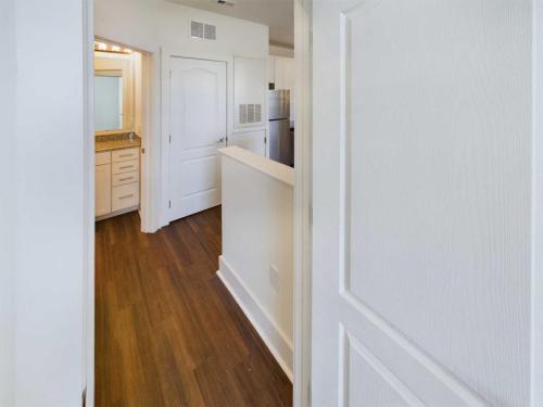 Apartments in Lebanon, IN View of a hallway with wooden flooring, leading to a bathroom on the left and a kitchen area towards the back. The walls and doors are white, complementing the overall bright and modern interior. Ideal for those seeking apartments for rent in Lebanon, Indiana.