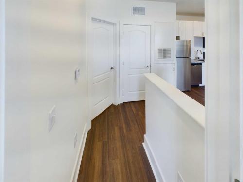 Apartments in Lebanon, IN A hallway in a modern apartment with white walls and wooden floors, leading to a kitchen area with stainless steel appliances. There are two closed doors on the left and one open passage on the right. Discover stylish living spaces like this among Apartments for Rent in Lebanon, Indiana.