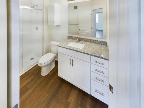 Apartments in Lebanon, IN A modern bathroom in one of the apartments for rent in Lebanon, Indiana, featuring a glass-enclosed shower, a toilet, a granite countertop sink, and white cabinetry with silver handles. The floor is made of wood.