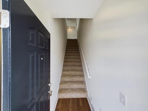 Apartments in Lebanon, IN Open black door revealing an interior with a carpeted staircase leading upward, white walls, and wooden flooring at the entrance.