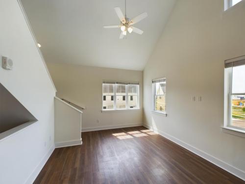 Apartments in Lebanon, IN A bright, empty room with white walls and a wooden floor. It features several windows, a ceiling fan, and a staircase to the left.