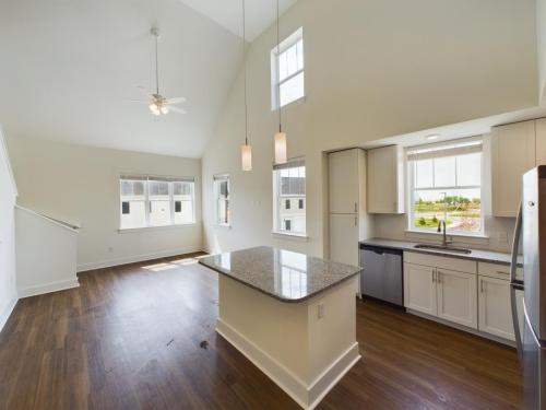 Apartments in Lebanon, IN A modern kitchen with white cabinets, granite countertops, and stainless steel appliances opens to a bright living area with hardwood floors, large windows, and high ceilings with ceiling fan.