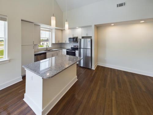 Apartments in Lebanon, IN Modern kitchen with stainless steel appliances, granite countertop island, wooden flooring, and white cabinets. Recessed and pendant lighting are present.