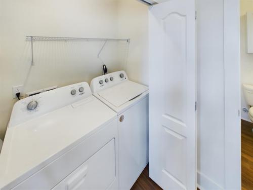 Apartments in Lebanon, IN A laundry room with a white washer and dryer, an open door partially blocking the view, a wire shelf above the appliances, and the edge of a bathroom visible to the right.