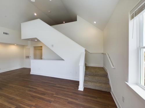 Apartments in Lebanon, IN Spacious room with wooden flooring, white walls, and a staircase leading to an upper level. Natural light enters through a window on the right.