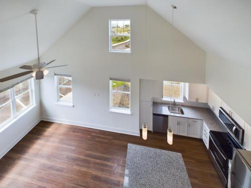 Apartments in Lebanon, IN A spacious open-floor living area with wooden flooring, light fixtures, a ceiling fan, and a modern kitchen featuring a granite island and stainless steel appliances, viewed from an elevated angle.