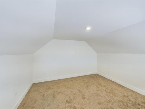 Apartments in Lebanon, IN An empty room with slanted ceilings, white walls, beige carpeting, and a recessed light on the ceiling.