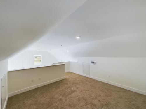 Apartments in Lebanon, IN A carpeted attic room with slanted white walls, a small window, and recessed lighting on the ceiling.