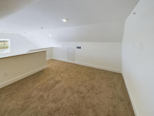 Apartments in Lebanon, IN A spacious, carpeted attic room with white walls and a small, closed door on one side. The room is well-lit with ceiling lights and a small window near the roof peak.