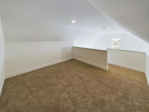 Apartments in Lebanon, IN A spacious, empty loft with slanted ceilings, beige carpet, and a small square window on the far wall allowing natural light into the white-painted room.