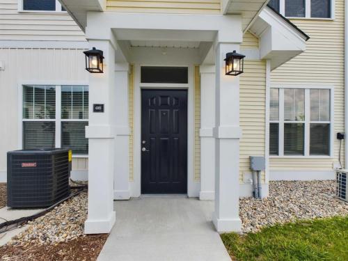 Apartments in Lebanon, IN A front entrance of a house with a black door, white pillars, and two wall-mounted lanterns. A small path leads to the door. An air conditioning unit is positioned to the left of the entrance.