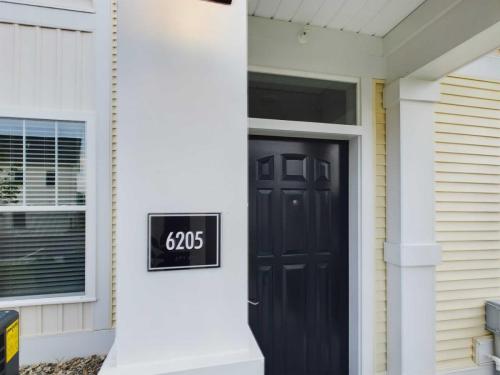 Apartments in Lebanon, IN A black front door of house number 6205, featuring a small rectangular sign displaying the number. The house exterior has beige siding and a white trim.