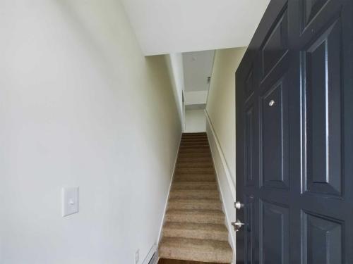 Apartments in Lebanon, IN Open black door revealing an interior staircase with beige carpet, white walls, and a hallway at the top.